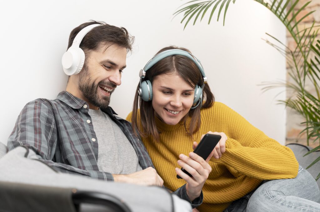 Happy couple both wearing headphones and looking at a phone.
