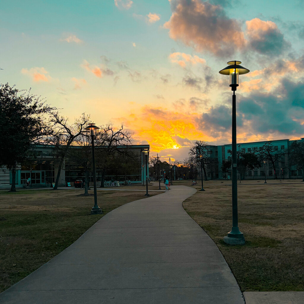 Sun setting against blue sky and few clouds on a college campus.